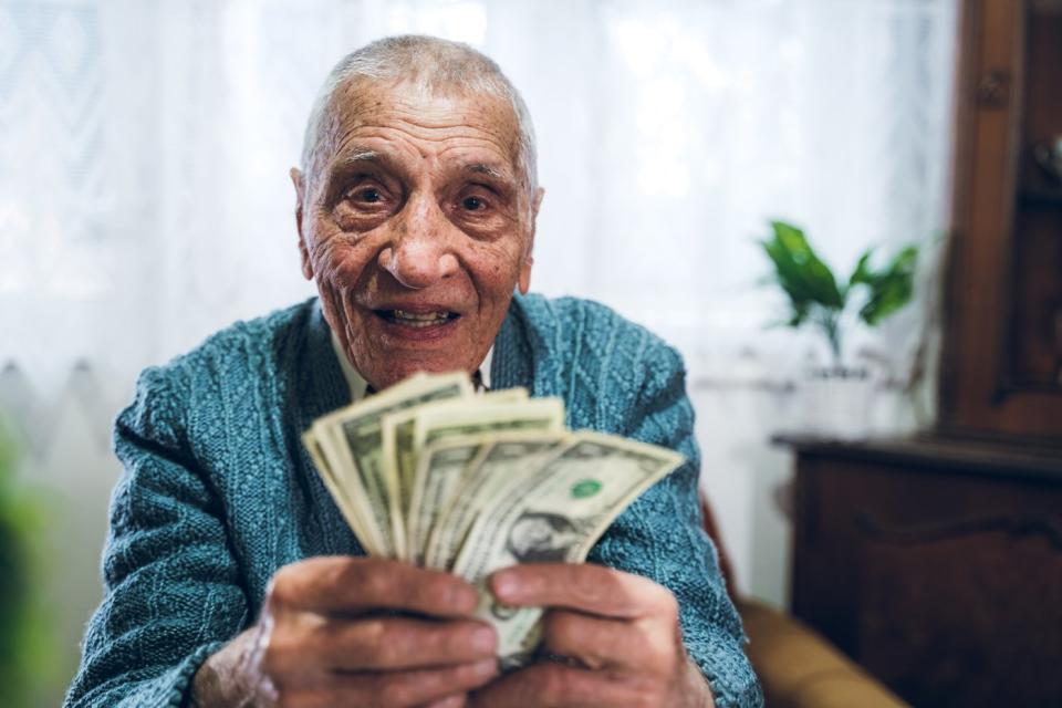 A seated person holding a fanned assortment of cash bills in their hands. 