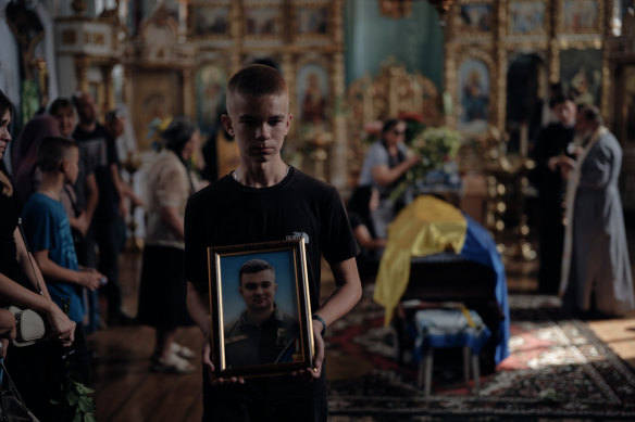 The son of Ukrainian F-16 pilot Oleksiy Mes holds a portrait of his late father during the rite of burial, on Thursday, the Day of Remembrance for Fallen Heroes.